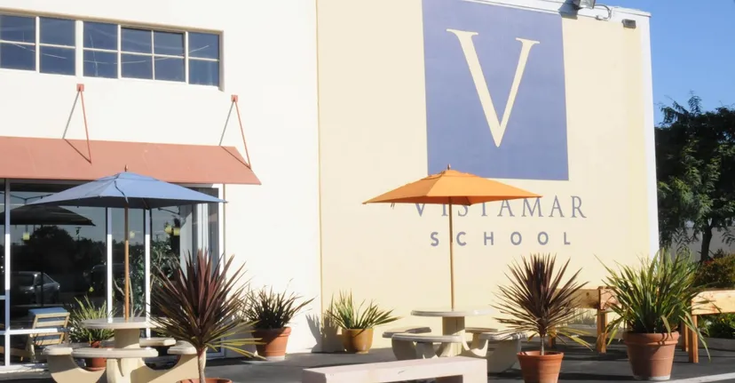L'area esterna della Vistamar School con tavoli, ombrelloni, piante in vaso e il logo della scuola sulla facciata dell'edificio.