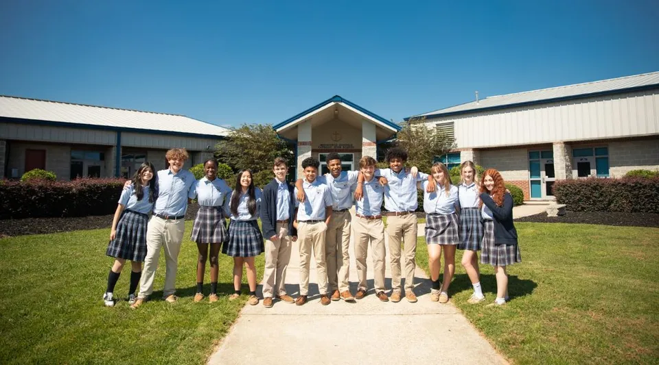 Un gruppo di studenti si trova davanti all'edificio scolastico della Monsignor Donovan Catholic High School sotto un cielo blu.