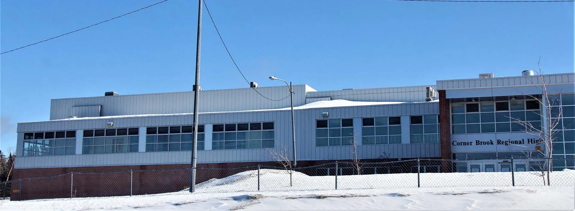 Il grande edificio industriale nel campus della Corner Brook Regional High School con il cielo limpido e la neve in primo piano.