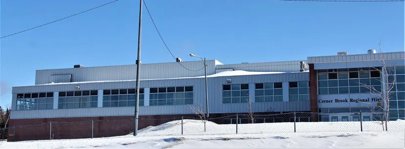 Il grande edificio industriale nel campus della Corner Brook Regional High School con il cielo limpido e la neve in primo piano.