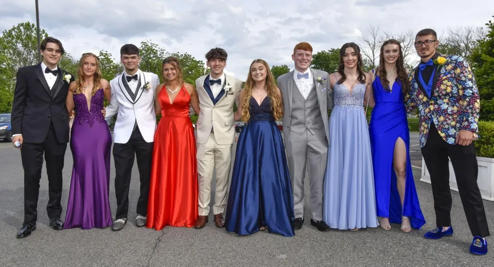 Un gruppo di studenti e studentesse della Wakatipu High School posa in abito formale all'aperto davanti ad alberi e a un cielo nuvoloso.