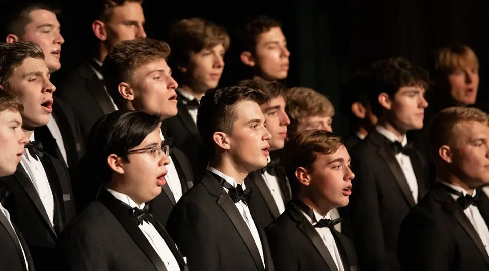 Un gruppo di studenti della McCallie School canta insieme durante un'esibizione sul palco.