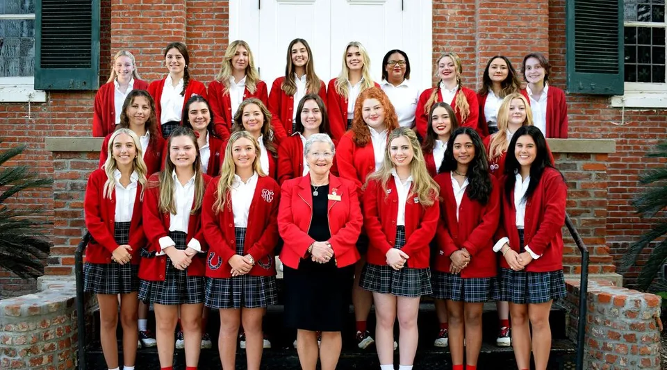 Un gruppo di studentesse in divisa rossa si trova davanti a un edificio in mattoni nel campus della Academy of the Sacred Heart.