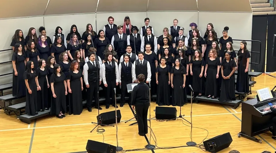 Un grande coro della Wyoming High School si trova sul palco e canta sotto la direzione di un direttore.