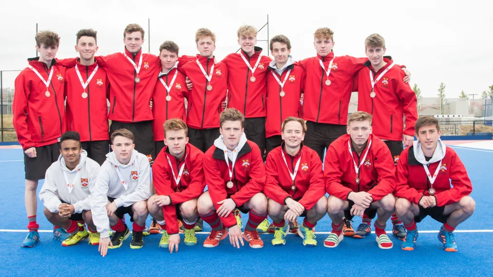 Una squadra sportiva della Kingston Grammar School posa con le medaglie su un campo sportivo blu.