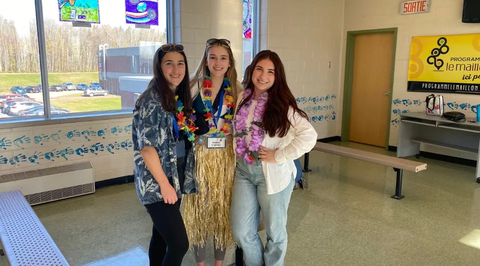 Tre studentesse sorridono nel corridoio della Carrefour de l’Acadie davanti ad armadietti e poster della scuola.