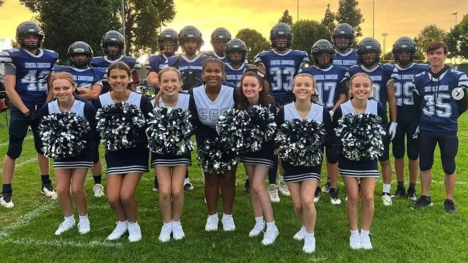 Studenti della Coastal Christian School posano insieme come giocatori di calcio e cheerleader su un campo d'erba al tramonto.