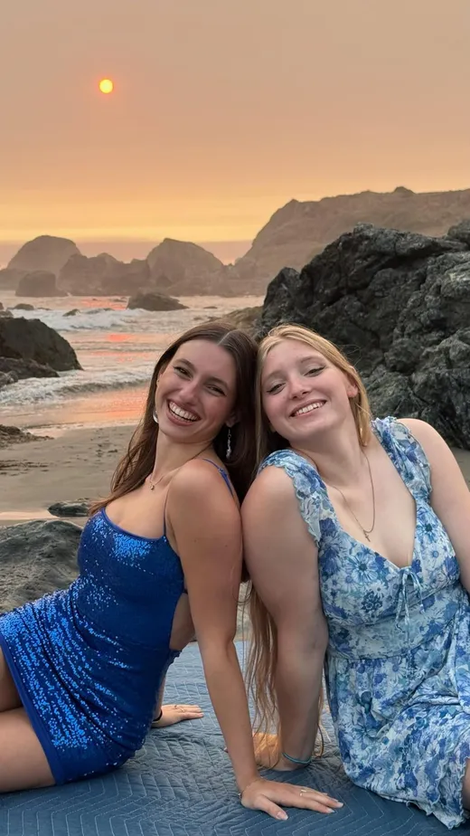 Due ragazze sorridenti sedute su una spiaggia al tramonto durante un anno all'estero