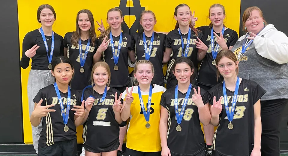 Un gruppo di giovani atlete della Drumheller Valley School posa con le medaglie davanti a uno sfondo giallo.