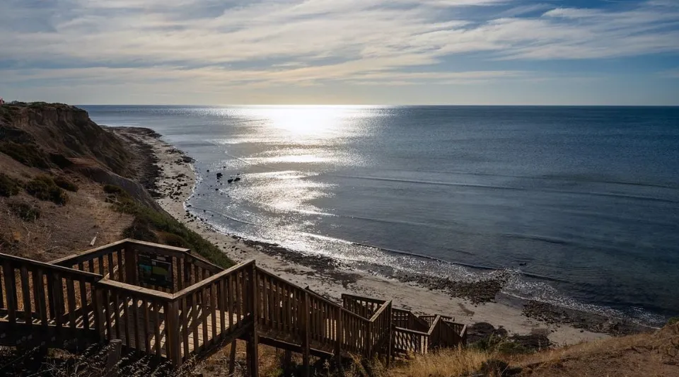 Una scala in legno porta alla spiaggia con onde dolci sotto un cielo nuvoloso nell'area della Seaview High School.