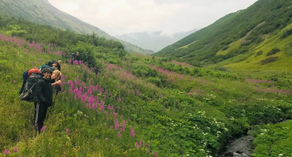 Un gruppo di studenti dell'Abbey College fa un'escursione attraverso una valle verde ricca di fiori selvatici e circondata da alte montagne.