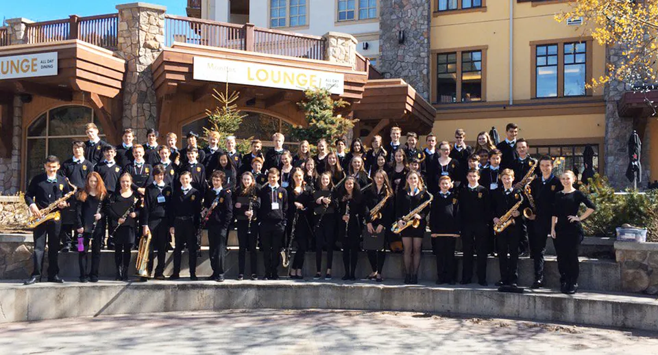 Un grande gruppo di persone in abito formale si riunisce all'esterno della Windsor Secondary School davanti ad edifici in legno.