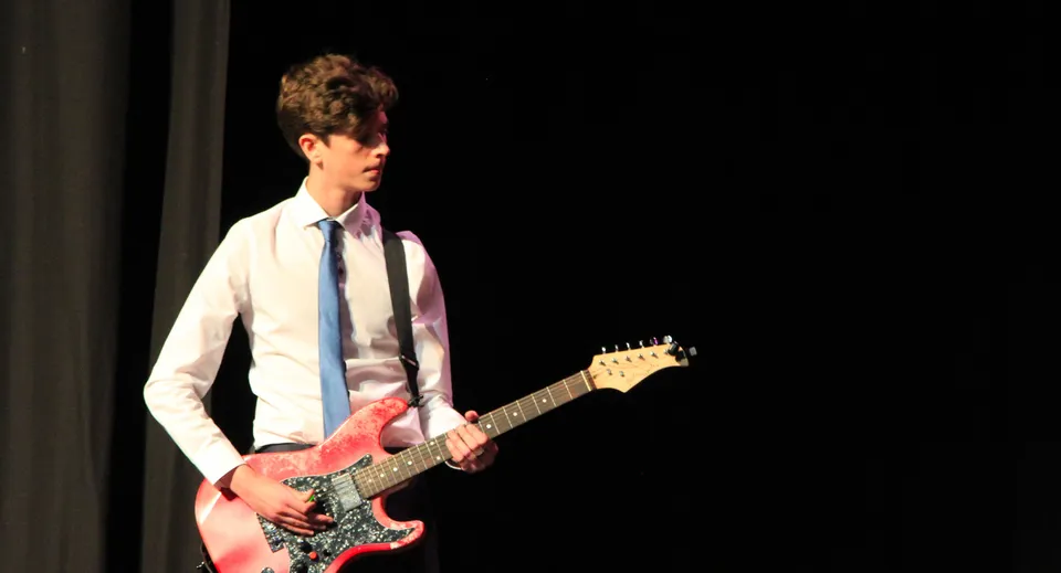 Una persona suona una chitarra elettrica su un palco buio alla Somerset Studio School.