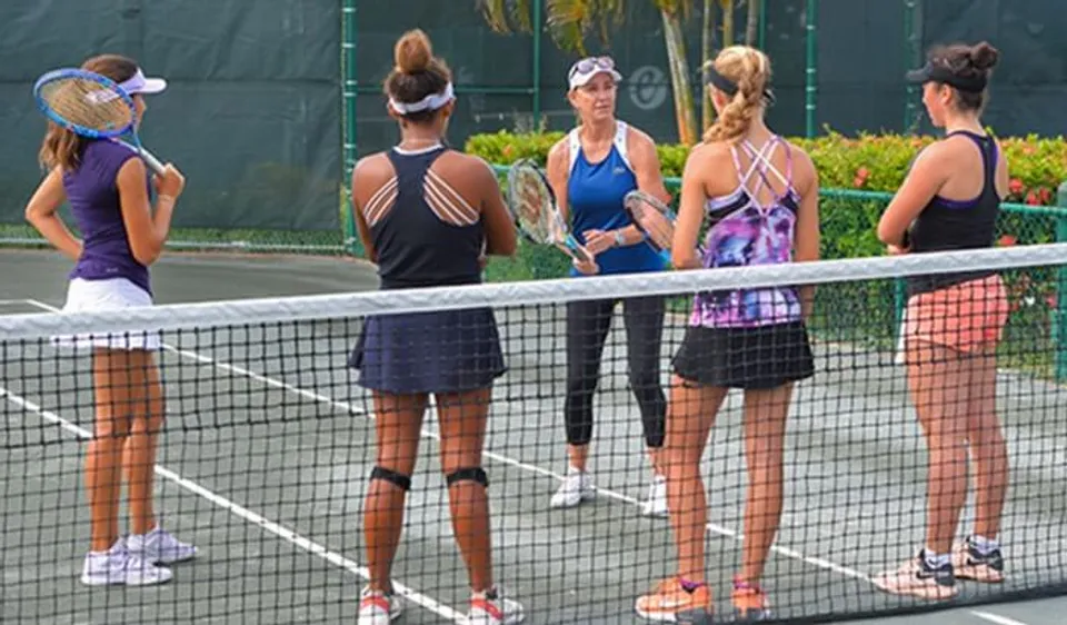 Un'allenatrice e quattro giocatrici della Evert Tennis Academy si trovano vicino alla rete da tennis.
