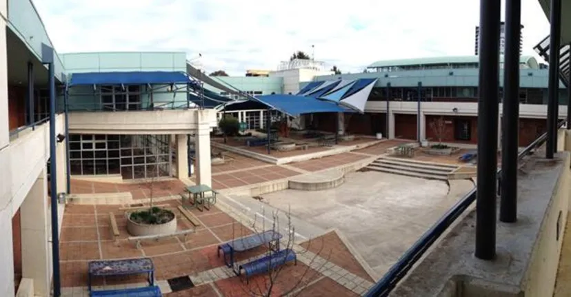 Un'area esterna moderna con edifici e sedute nel campus della UC-Lake Ginninderra School su uno sfondo urbano.