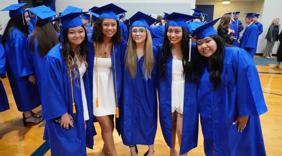 Un gruppo di giovani donne in toghe blu da laurea è insieme nel campus del Urbandale Community School District.
