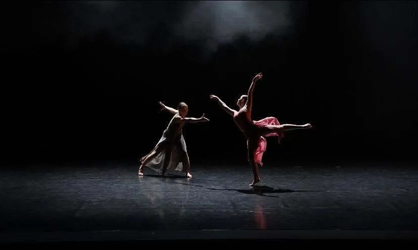 Dos bailarinas de la Asquith High School bailan con vestidos en un escenario oscuro bajo los focos.