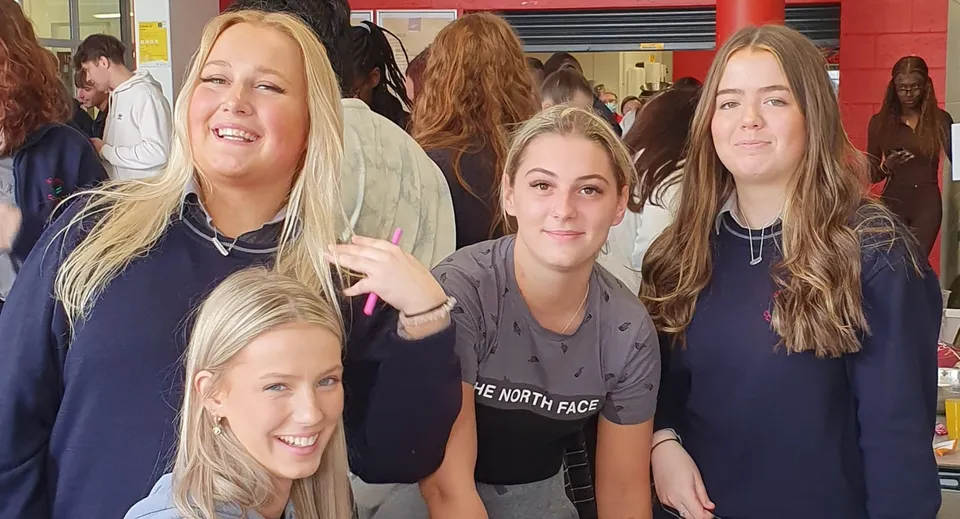 Un gruppo di studentesse sorridenti indossa felpe blu al coperto nel campus del St. Conleths College.