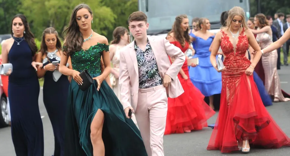 Un gruppo di studenti e studentesse del St. Tiernan’s College vestiti elegantemente si raduna all'aperto davanti ad alberi ed edifici.