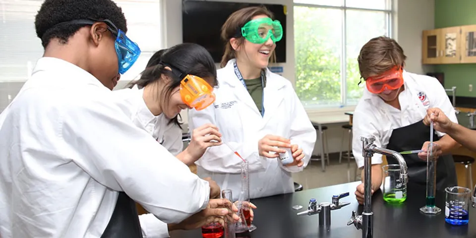 Quattro studenti della Fulton Science Academy con camici da laboratorio e occhiali protettivi eseguono esperimenti in laboratorio.