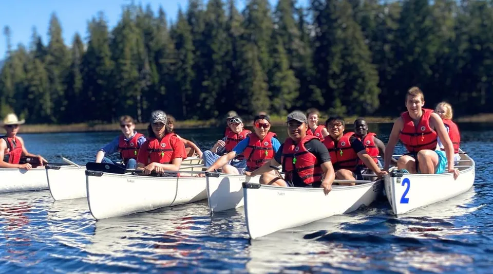 Studenti della Caledonia Secondary School con giubbotto di salvataggio rosso siedono su piccole barche bianche in un lago in una zona boschiva.