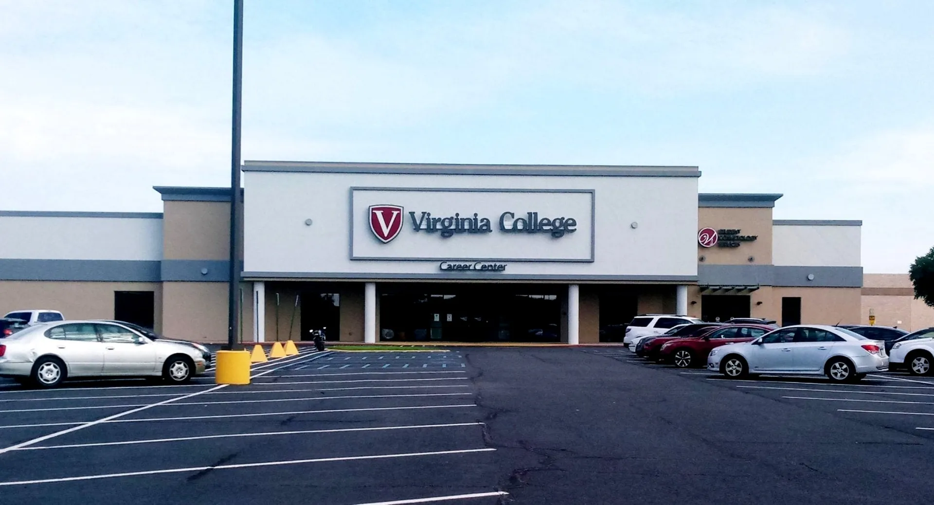 L'edificio esterno del Virginia College con una grande insegna e un parcheggio in primo piano è visibile sotto un cielo limpido.