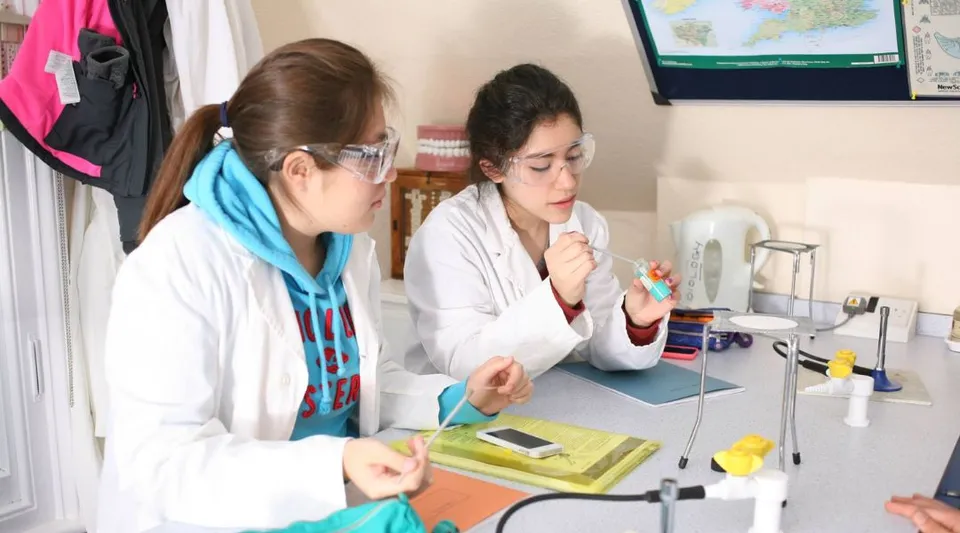 Due studentesse del St. Andrew’s College Cambridge lavorano insieme in laboratorio a esperimenti scientifici.