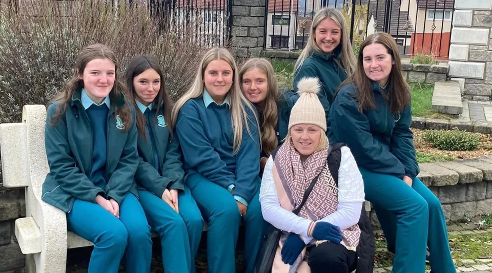 Un gruppo di studentesse sta davanti a un muro di pietra e una staccionata in legno nel terreno della St. Louis Secondary School.