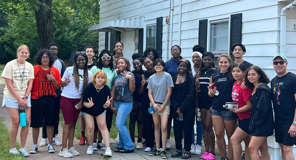 Un gruppo di studenti e studentesse davanti all'edificio della Connecticut IB Academy con un paesaggio verde sullo sfondo.