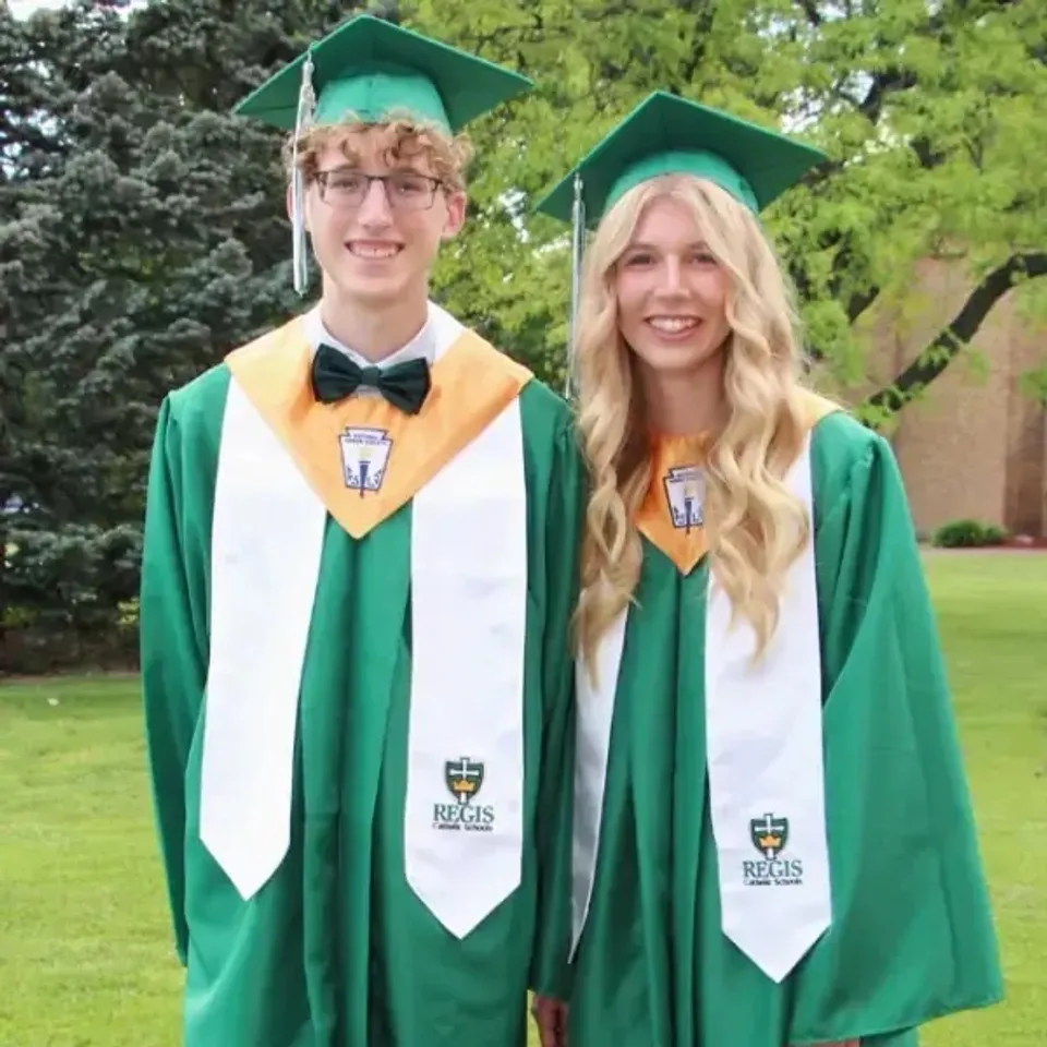 Due diplomati della Regis High School con toga e tocco verdi sorridono all'aperto.