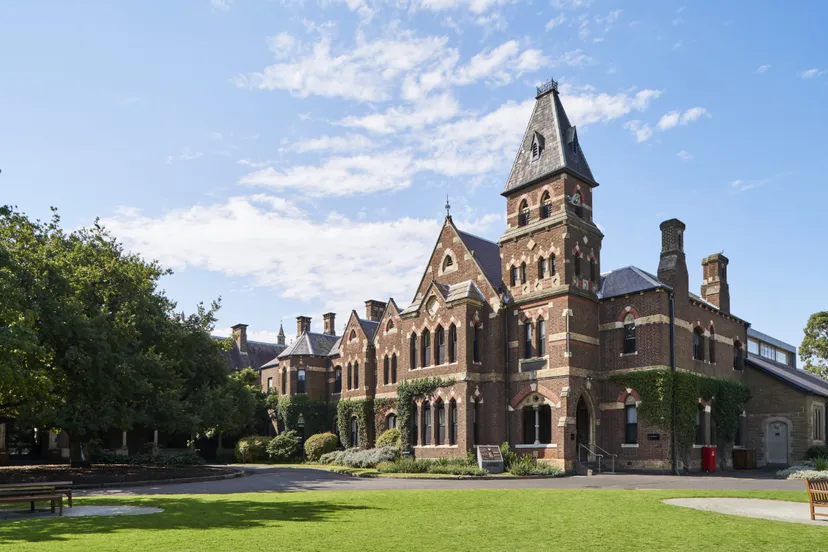 Il storico edificio in mattoni con un'alta torre nel campus del Trinity College è circondato da alberi verdi.