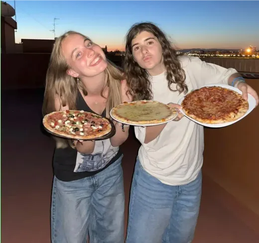 Zwei Mädchen zeigen bei Sonnenuntergang frisch gebackene Pizzen auf einer Terrasse in Spanien