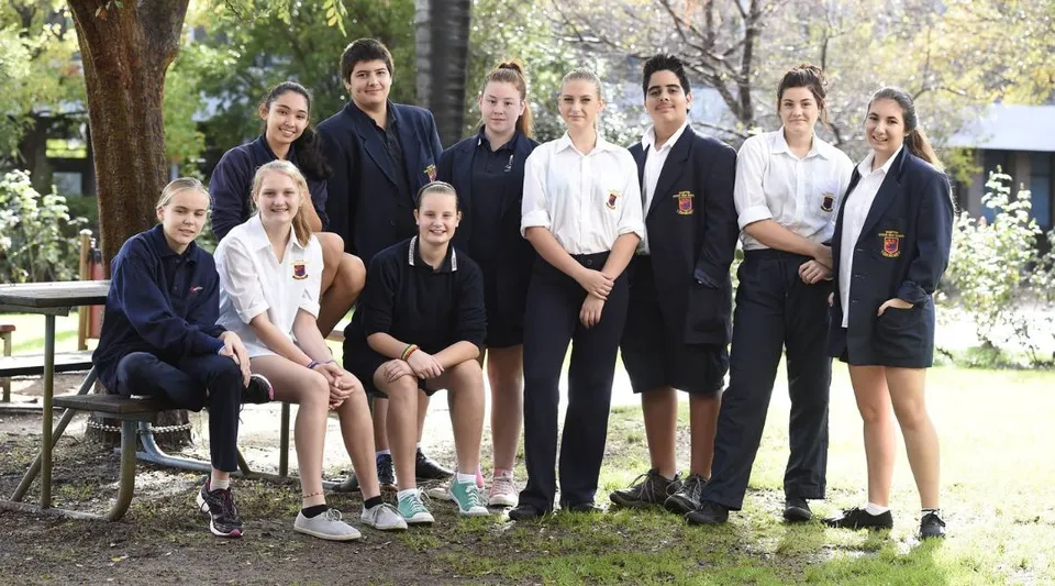 Un gruppo di studenti e studentesse si trova in piedi e seduto insieme in un'area esterna naturale della Hampton Senior High School.