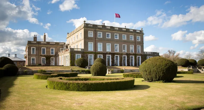 L'edificio principale a più piani della Queen Margaret's School for Girls con un pennone rosso sullo sfondo e un giardino ben curato in primo piano.