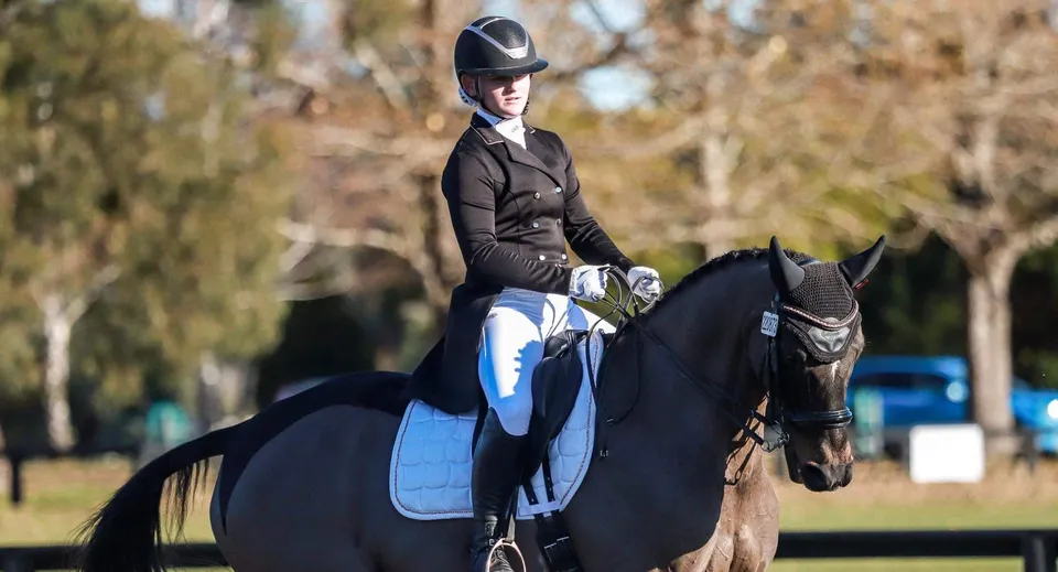 Una studentessa della Burnside High School cavalca un cavallo nero all'aperto con alberi sullo sfondo.