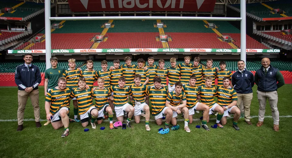 Un gruppo di studenti e studentesse con maglie a righe posa sul campo sportivo del Christ College davanti allo stadio.