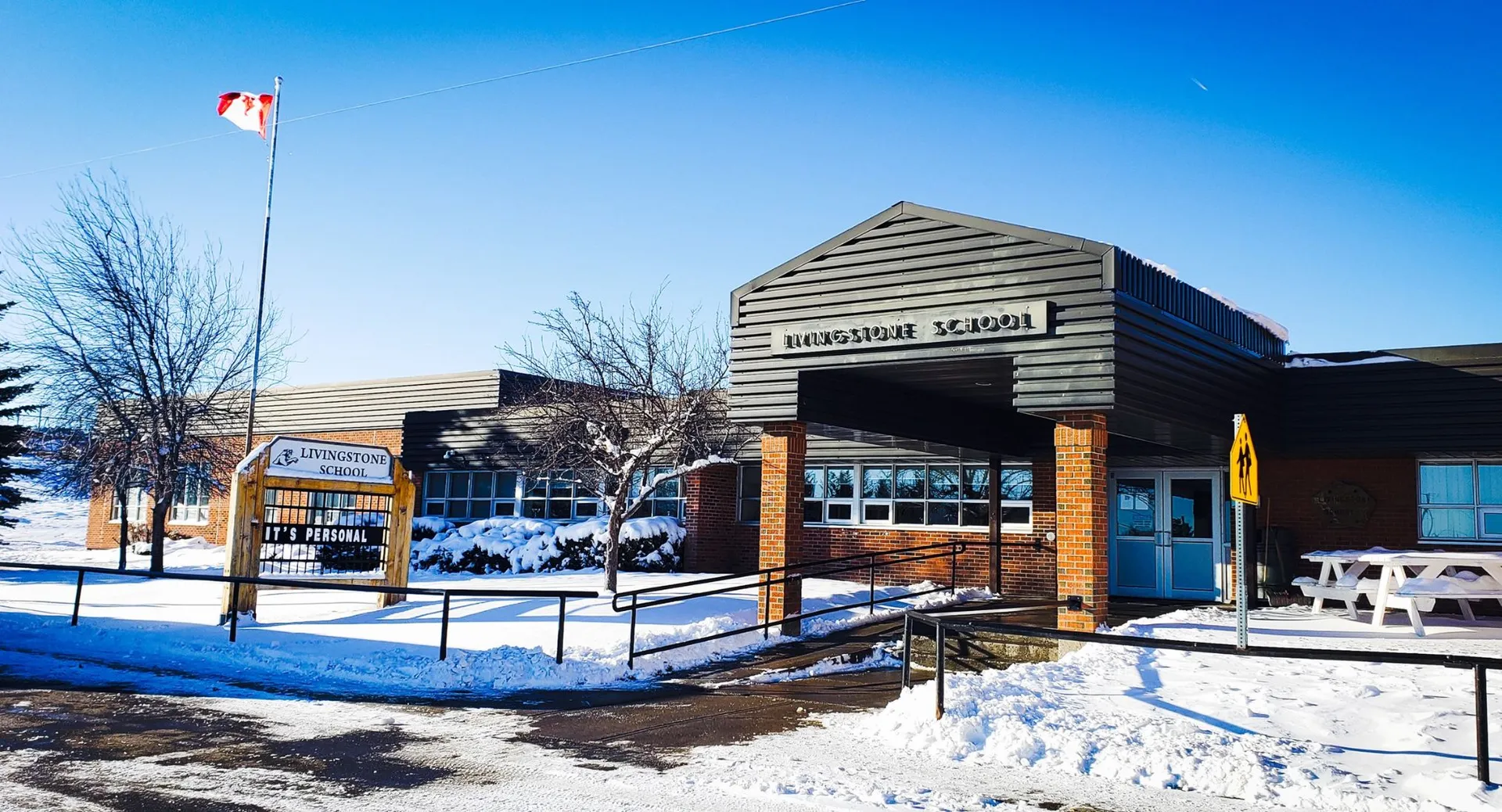 L'edificio scolastico in legno della Livingstone School si trova in un paesaggio innevato con alberi spogli e cielo blu.