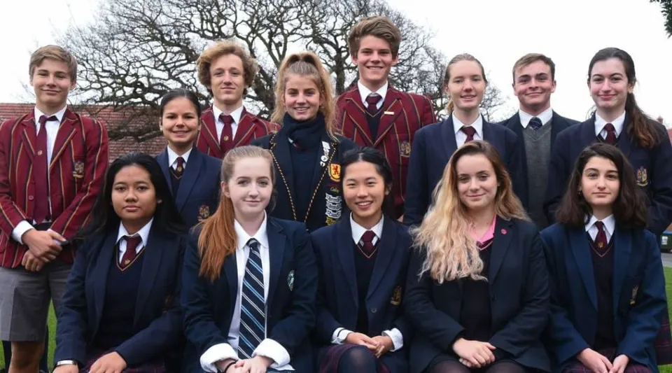 Un gruppo di studenti in divisa scolastica si trova davanti ad alberi spogli nel terreno del Scotch Oakburn College.