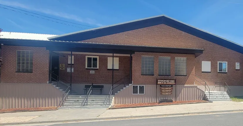 L'edificio in mattoni a due piani della Huntington High School con tetto a falde e scalinata d'ingresso lungo una strada con cavi elettrici.