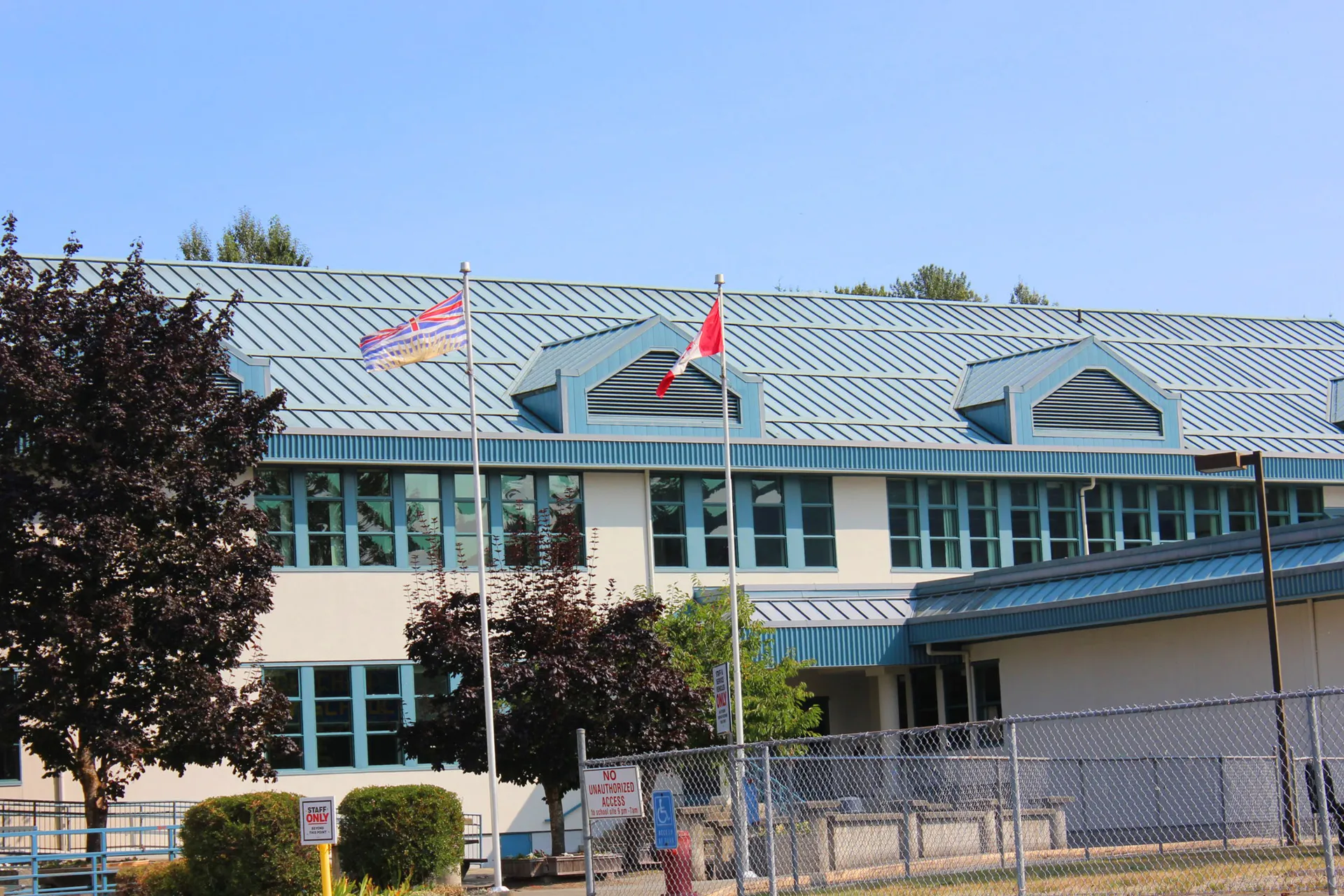 L'edificio a più piani con tetto in metallo verde della Lake Cowichan Secondary School è circondato da alberi e da una recinzione.