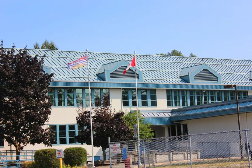 L'edificio a più piani con tetto in metallo verde della Lake Cowichan Secondary School è circondato da alberi e da una recinzione.