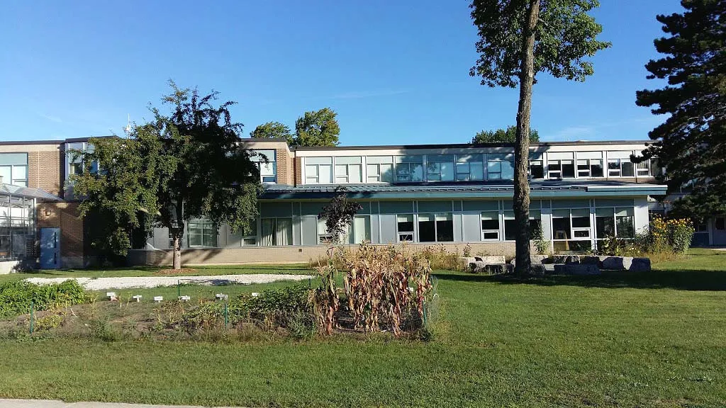 El edificio moderno del Stayner Collegiate Institute está rodeado de césped cuidado y árboles en primer plano.