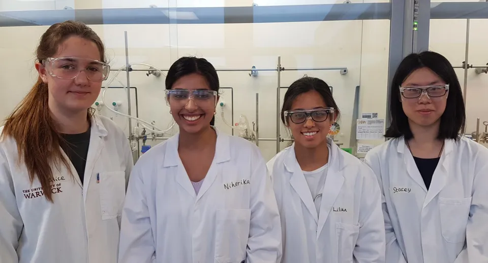 Quattro studenti della Sevenoaks School in camice bianco in un laboratorio con apparecchiature scientifiche.