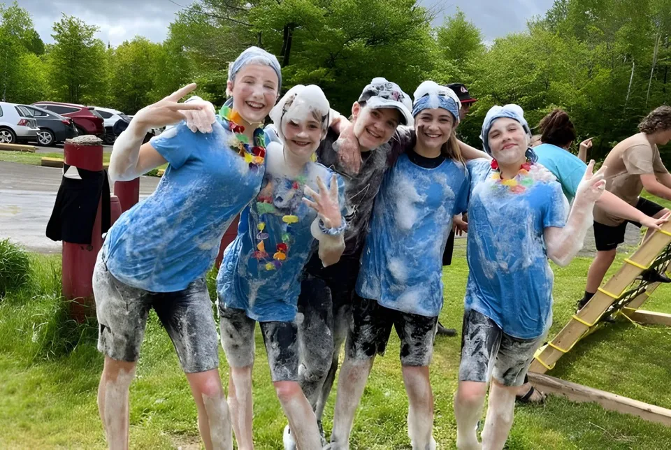 Un gruppo di persone con magliette batik colorate sta all'aperto tra alberi e prato nell'area della École Aux quatre vents.