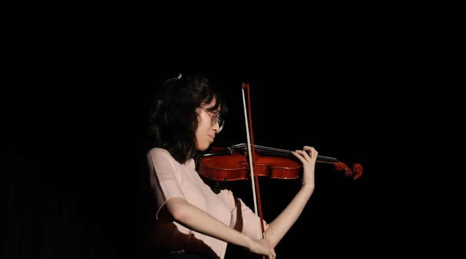 Una studentessa della Port Hacking High School suona il violino in una stanza scarsamente illuminata.