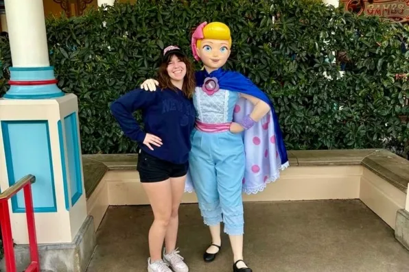 Chica sonriente posando junto a un personaje disfrazado de Bo Peep en un parque temático