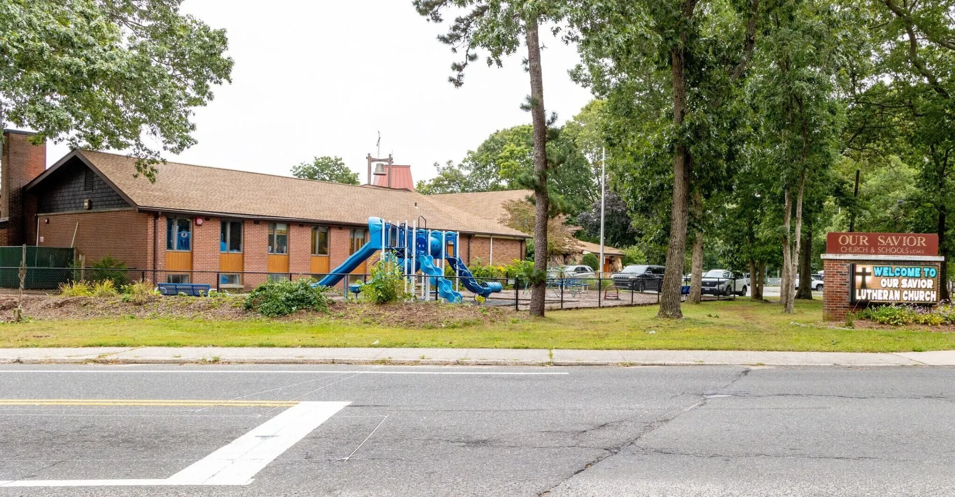 L'edificio in legno a due piani della Our Savior New American School è circondato da alberi verdi e si trova su una strada pavimentata.