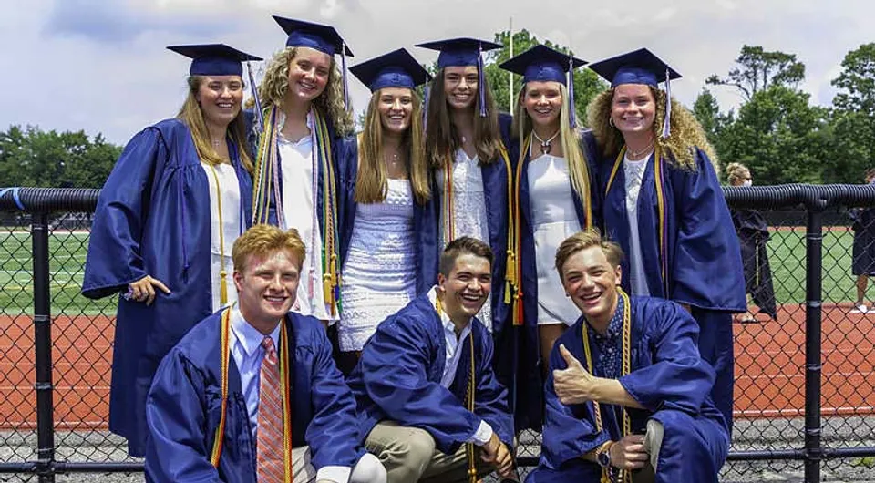 Un gruppo di diplomati della Chatham Kent Secondary School è davanti a un campo sportivo recintato.