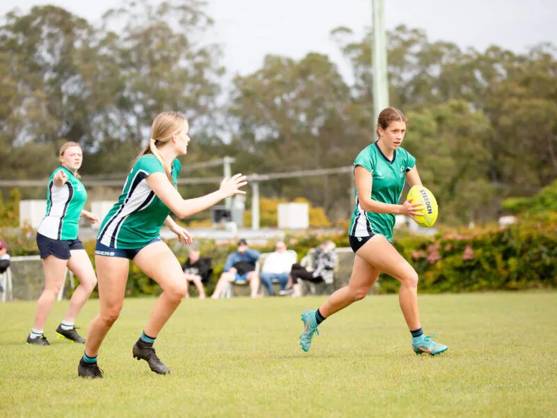 Estudiantes del Matthew Flinders Anglican College juegan en el campo de deportes rodeados de árboles y vegetación.