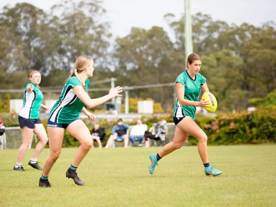 Studenti del Matthew Flinders Anglican College giocano sul campo sportivo circondato da alberi e vegetazione.